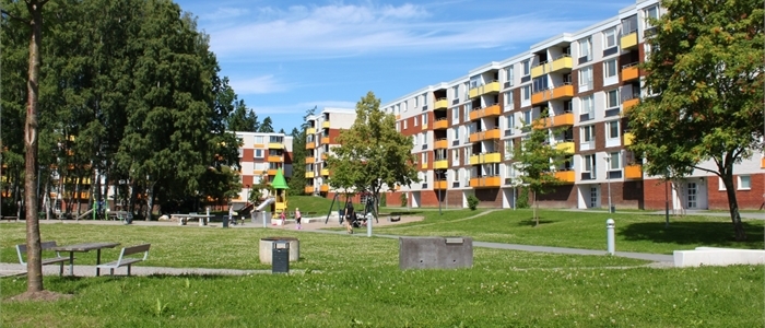 Lägenheter med balkonger och en stor gräsmatta nedanför som bland annat innehåller bänkar och gungor.
