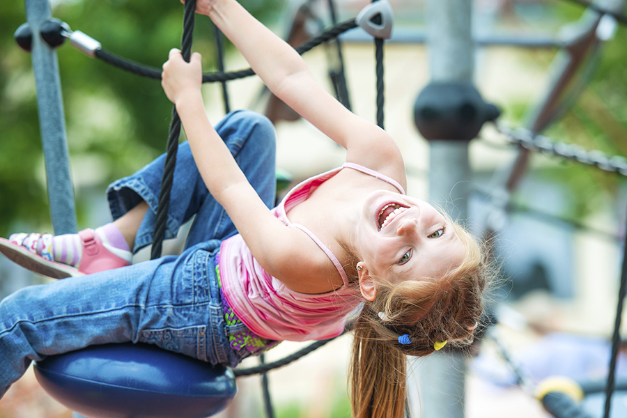 En lekande flicka hänger upp och ned i en klätterställning.