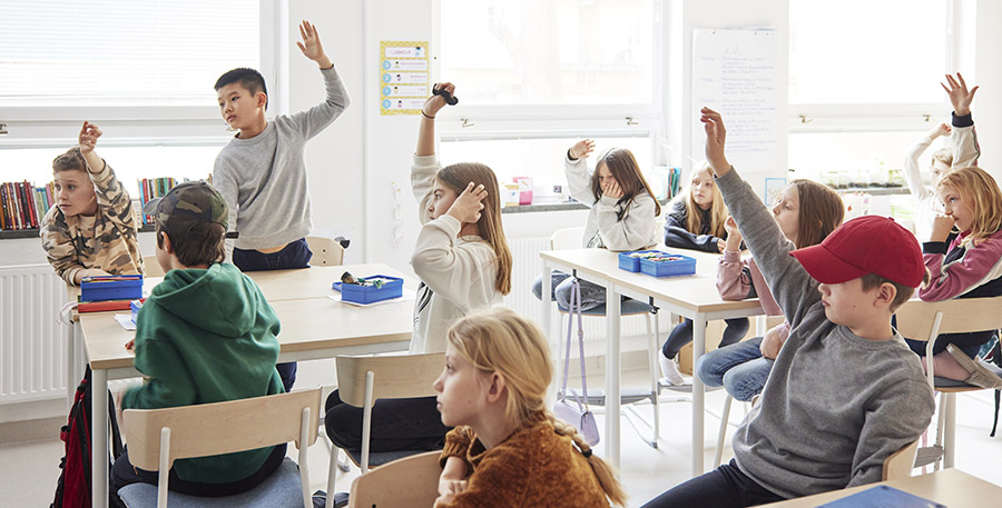 Elever i ett klassrum, några räcker upp handen.