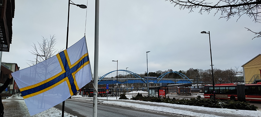 Sverigefinska flaggan i vit, gul och blå färg håller på att hissas upp på en flaggstång.