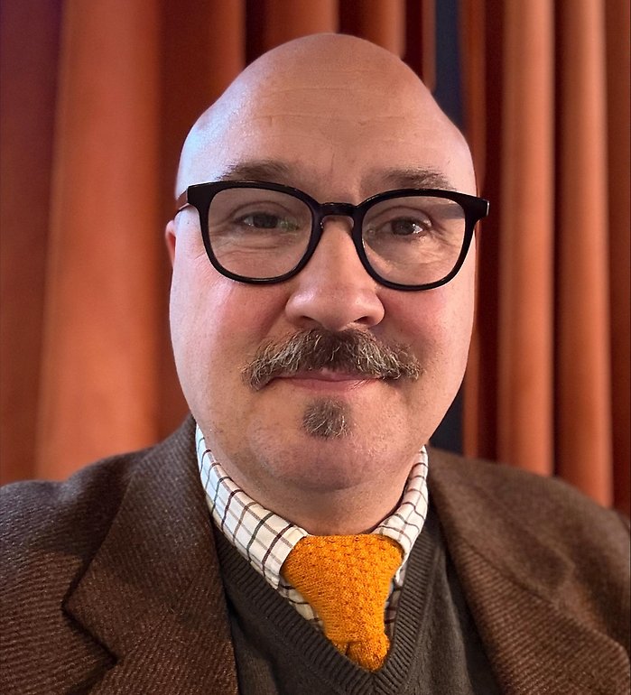 Bild på Johan. Han har glasögon och brun kavaj.