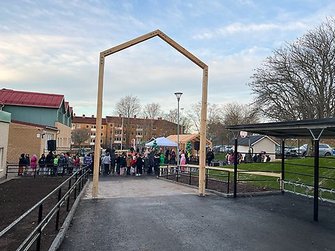 På bild syns en av skolans entréer med ett nytt cykelställ.I bakgrunden syns en grupp glada barn ska delta på invigningen, som ger en känsla av aktivitet och liv på skolområdet.