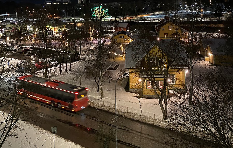 En röd SL-buss passerar vid Järnvägsparken och stationsområdet i Väsby. 