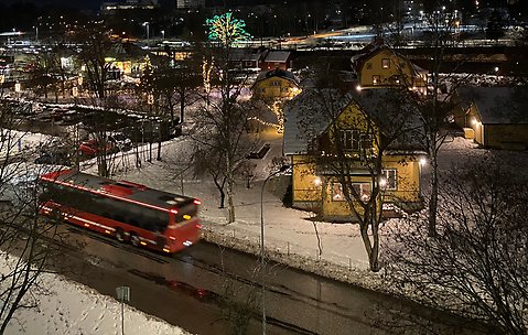 En röd SL-buss passerar vid Järnvägsparken och stationsområdet i Väsby. 