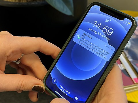 På bild syns en persons händer som håller i en telefon och mobilskärm med ett levererat sms. 