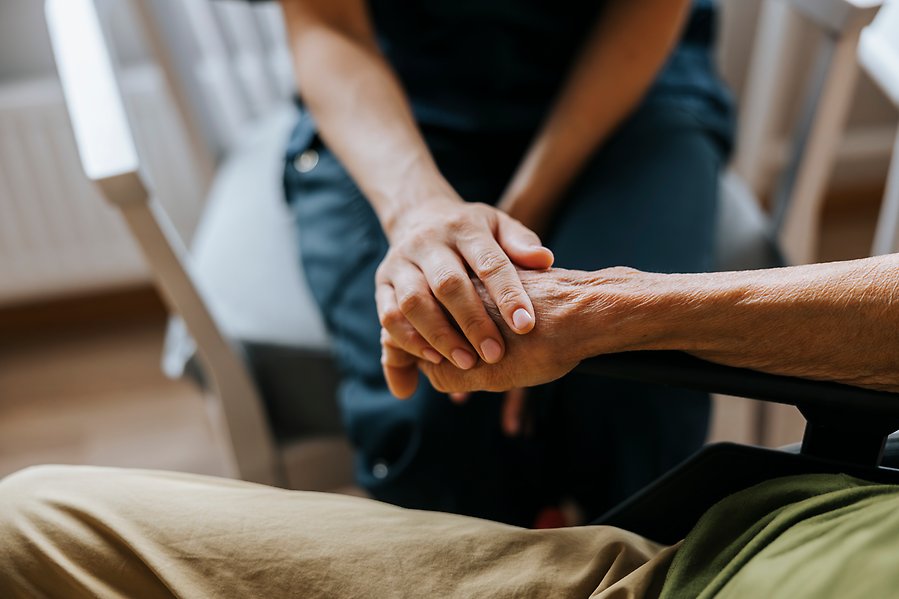 Närbild på vårdanställd som håller en äldre person i handen.