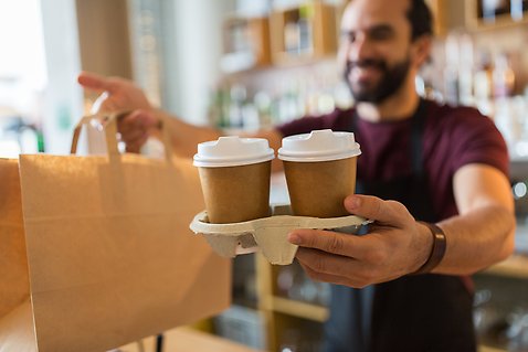 En caféanställd serverar två koppar kaffe till en kund. Foto: Mostphotos