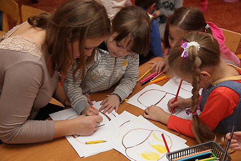 Tre barn sitter vid ett bord och ritar tillsammans med en pedagog. 